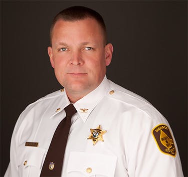 Portrait of a white male with neatly trimmed hair in a white sheriff's shirt and dark brown tie 👔.